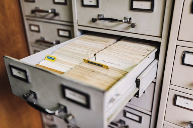 A photograph of a metal filing cabinet, one drawer open, full of cardboard index cards.